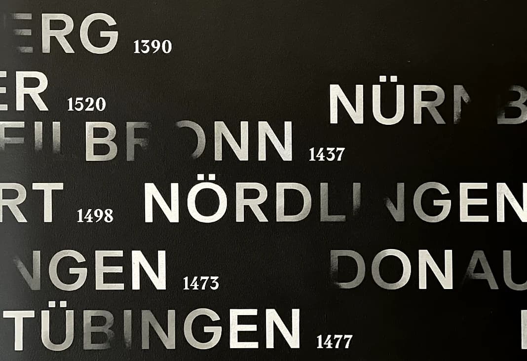 Weiße Schrift auf dunklem Grund, teils ausgebleicht, vom Lesen wieder sichtbar, zwischen Verschwinden und Erinnerung.