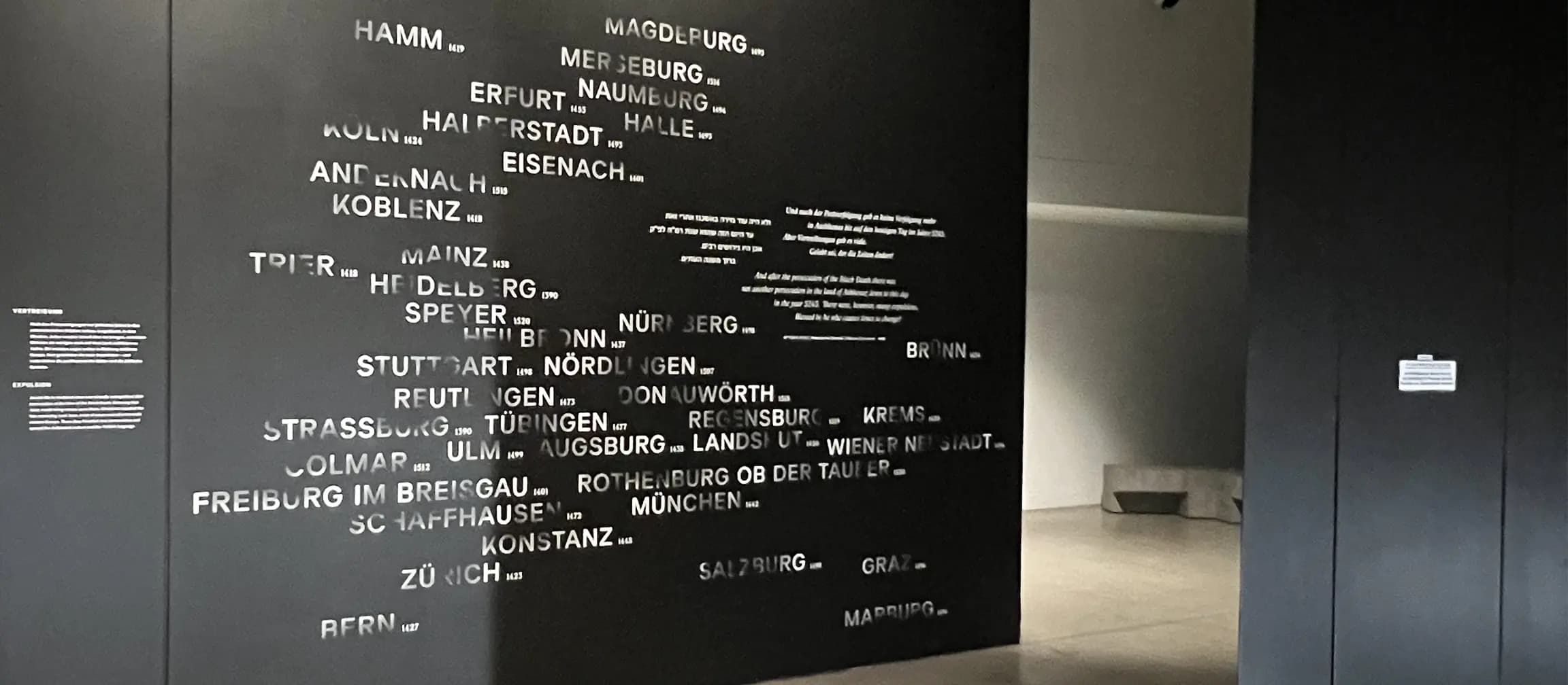 Weiße Schrift auf dunklem Grund, teils ausgebleicht, vom Lesen wieder sichtbar, zwischen Verschwinden und Erinnerung.